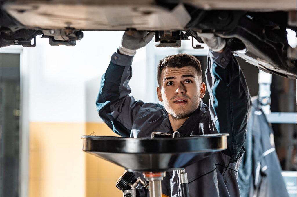 Man in a garage working underneath a raised car