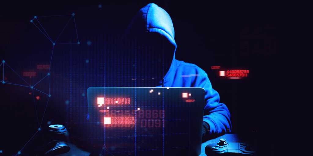 Hooded figure in a dark room using a laptop, symbolising cybercrime and data hacking, with digital code and network graphics overlaid on the image.
