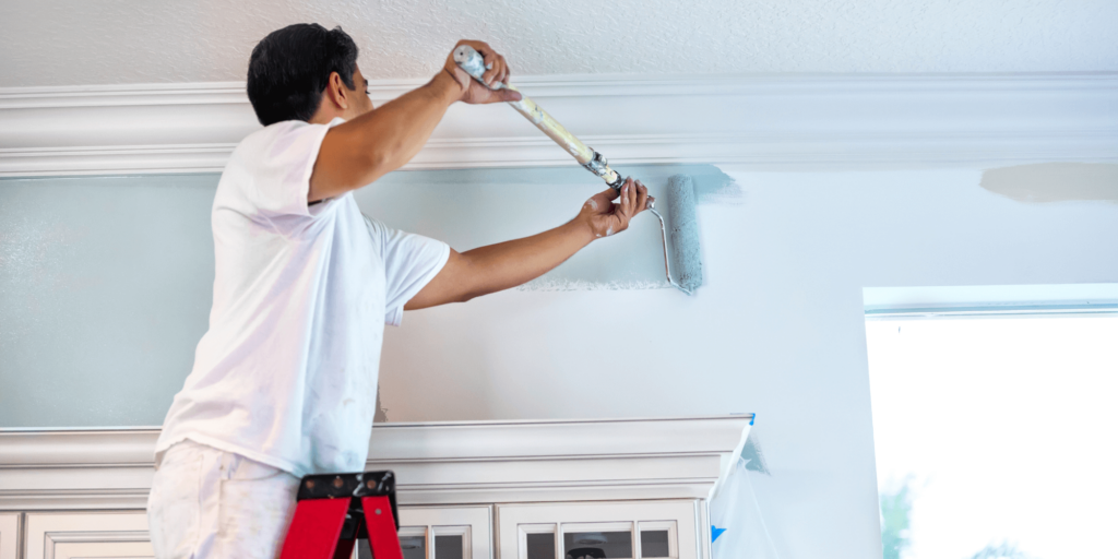 Painter applying a smooth coat of paint to a residential interior wall using a roller brush.