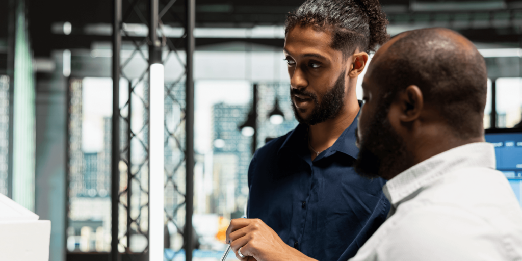 Two men in a modern office environment having a focused conversation while reviewing work.